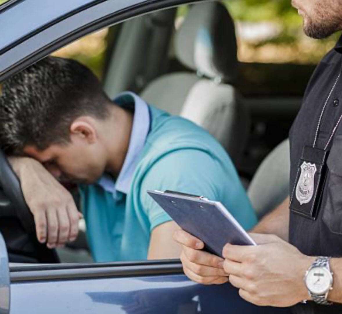 A man is sitting in the driver 's seat of his car while another person looks on.